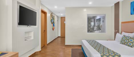 Habitación de hotel con una cama grande, televisor de pantalla plana montado en la pared, piso de madera y ventana con vistas.