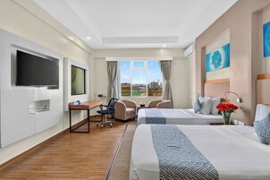 Quarto de hotel com duas camas, uma escrivaninha, uma cadeira, uma televisão e uma janela com vista.