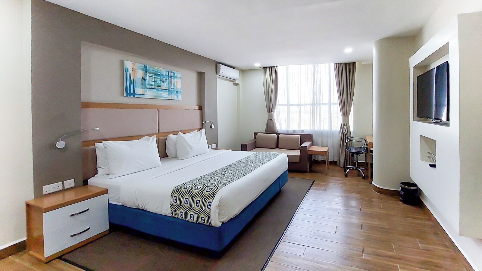 Une chambre d’hôtel comprenant un lit, une table de chevet, une chaise, une télévision et une fenêtre avec des rideaux.