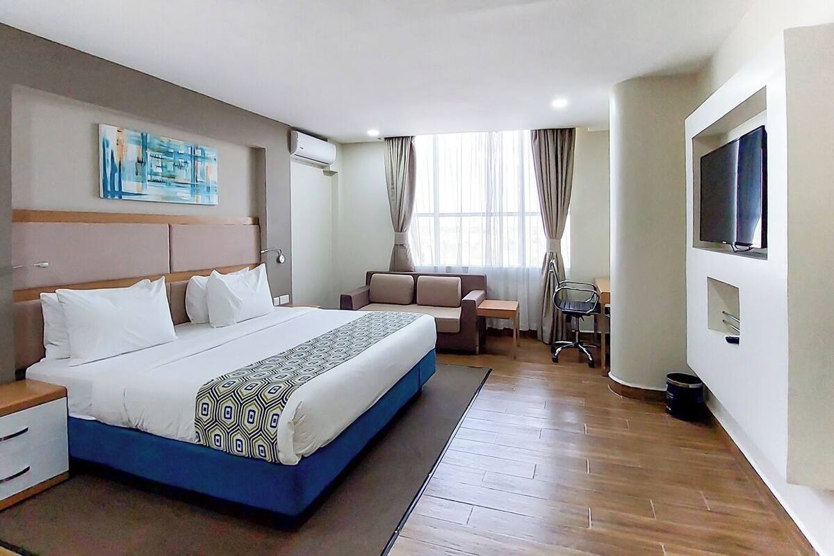 Une chambre d’hôtel comprenant un lit, une table de chevet, une chaise, une télévision et une fenêtre avec des rideaux.