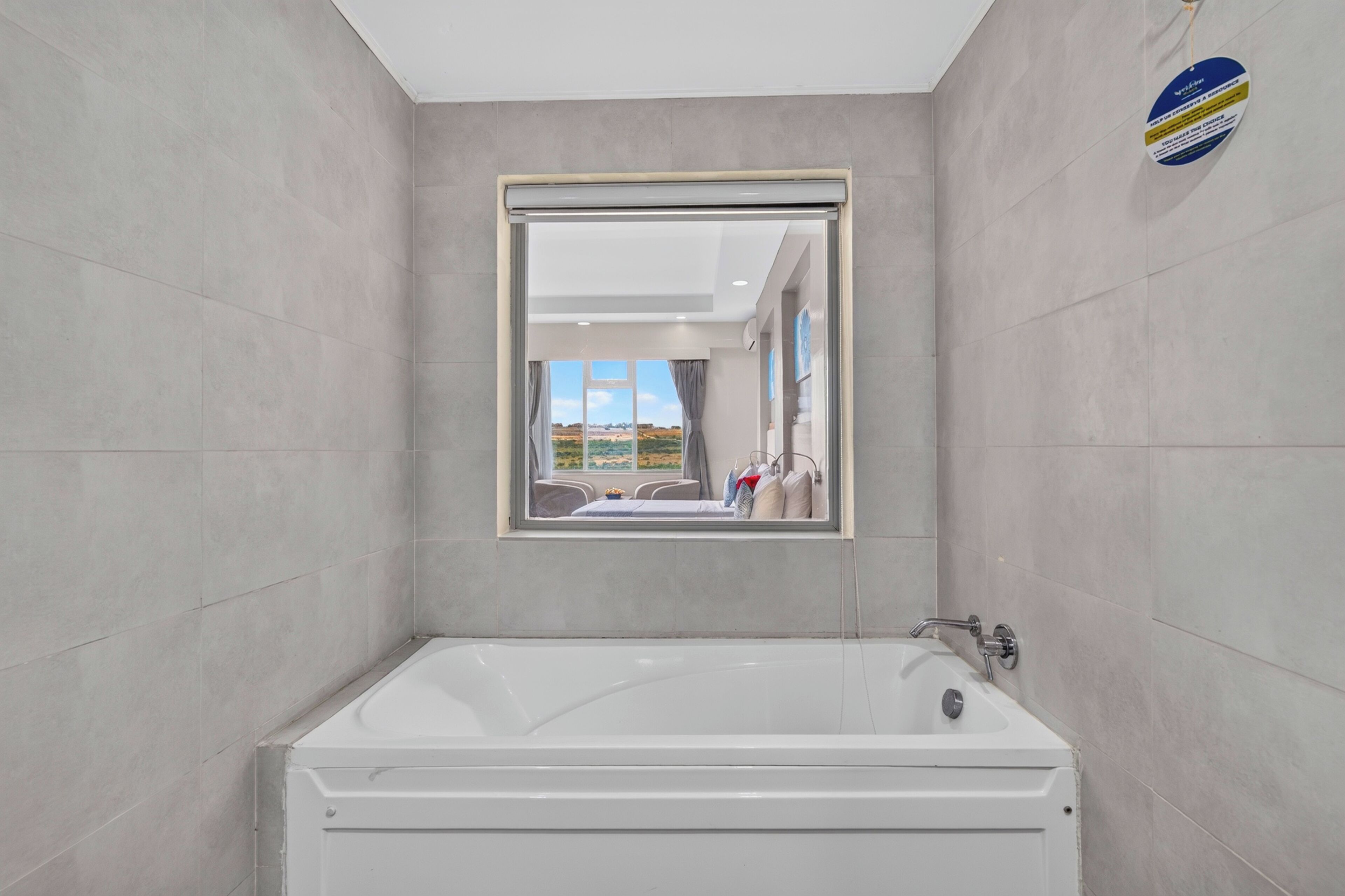 A modern bathroom with a large bathtub, a mirror, and a view of the outdoors.