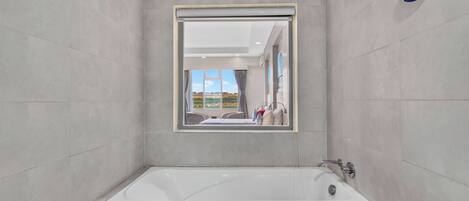 A modern bathroom with a large bathtub, a mirror, and a view of the outdoors.