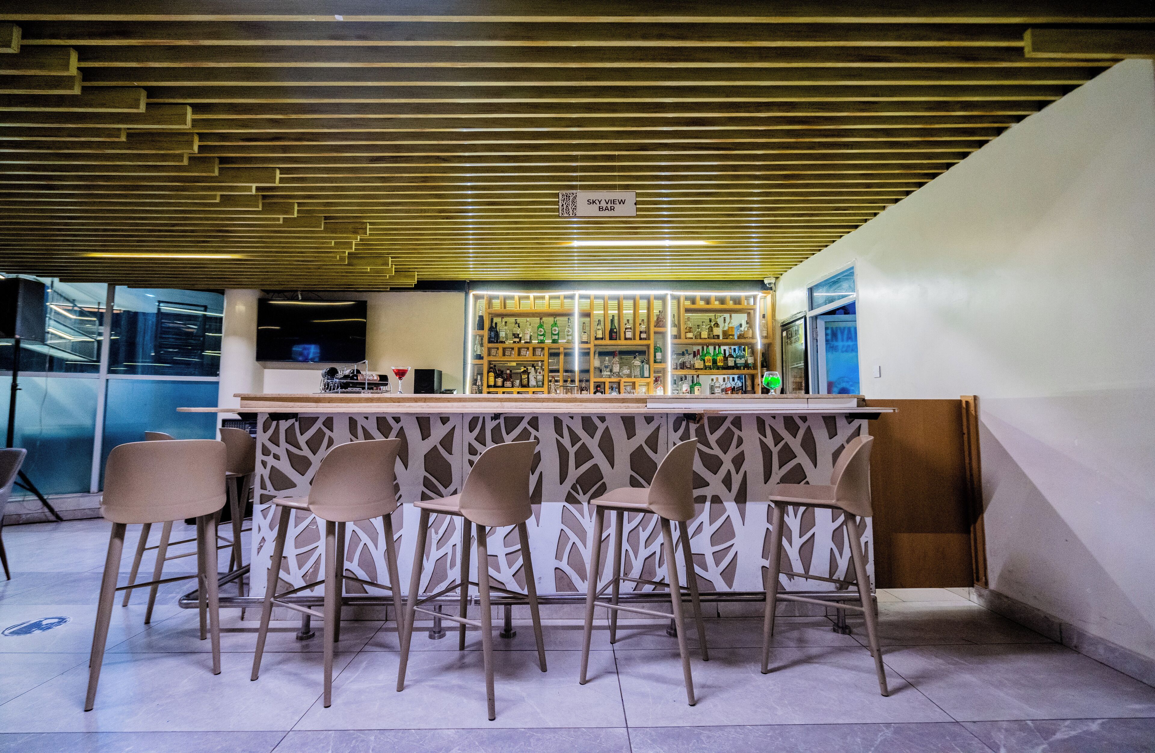A bar area with a modern design, featuring a wooden ceiling, a bar counter, and several bar stools.