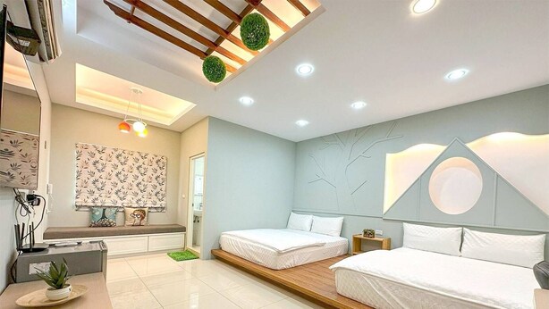A modern bedroom with two beds, a built-in bench, a ceiling with recessed lighting, and a wall with a geometric design.