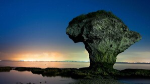 A large rock formation with a hole in the middle, surrounded by calm water and a sunset in the background. - Xiaoliuqiu 1302 Seaview Guesthouse (Liuqiu)