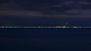 A nighttime view of a coastline with a distant city skyline.
