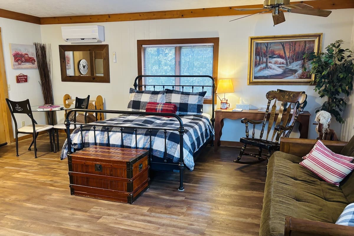 Ein gemütliches Zimmer mit einem Bett, einem Schaukelstuhl, einer Holzkiste und einem Schreibtisch mit Lampe.