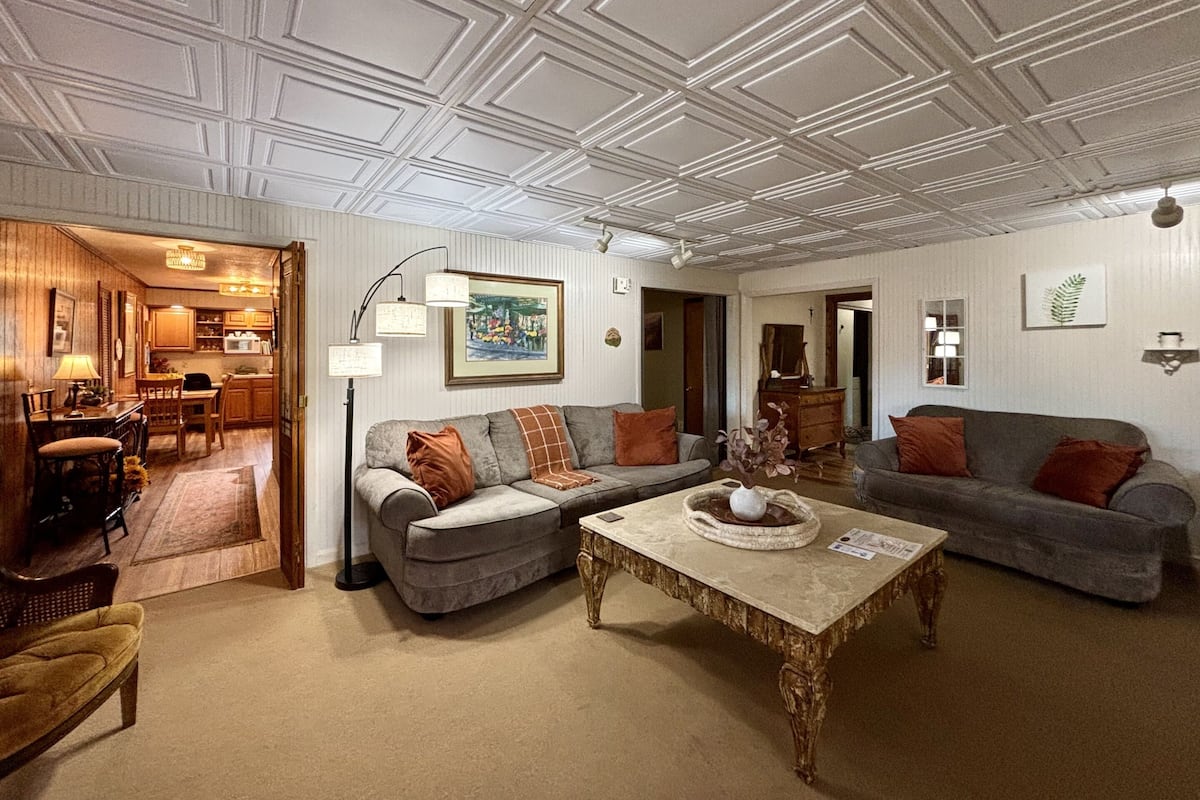 Ein geräumiges Wohnzimmer mit hohen Decken, zwei Sofas, einem Couchtisch und einer Essecke mit Holzmöbeln.