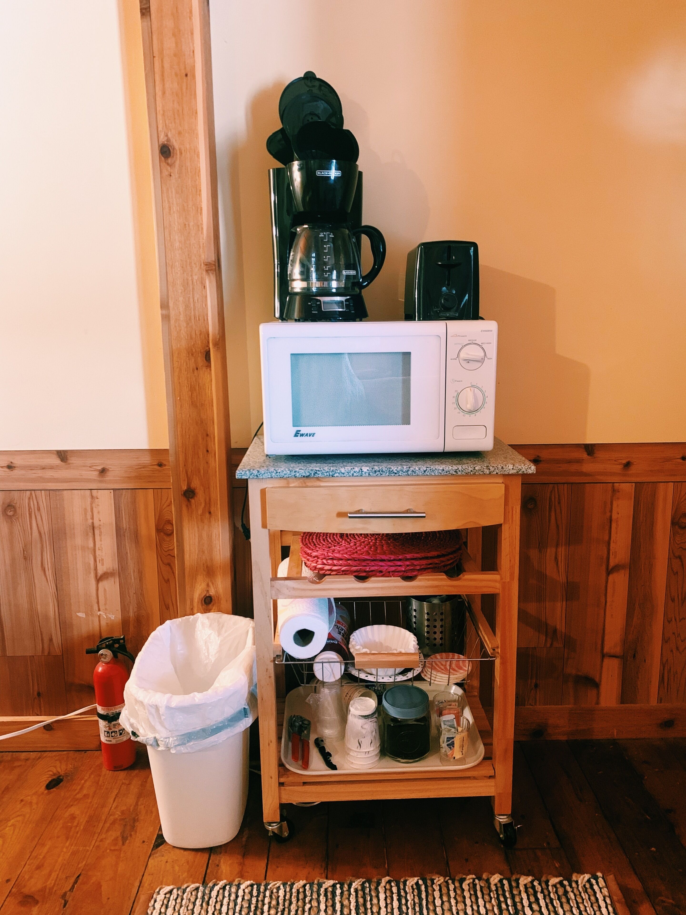 Eine Küchenzeile mit einer Mikrowelle, einer Kaffeemaschine und einem Mülleimer.
