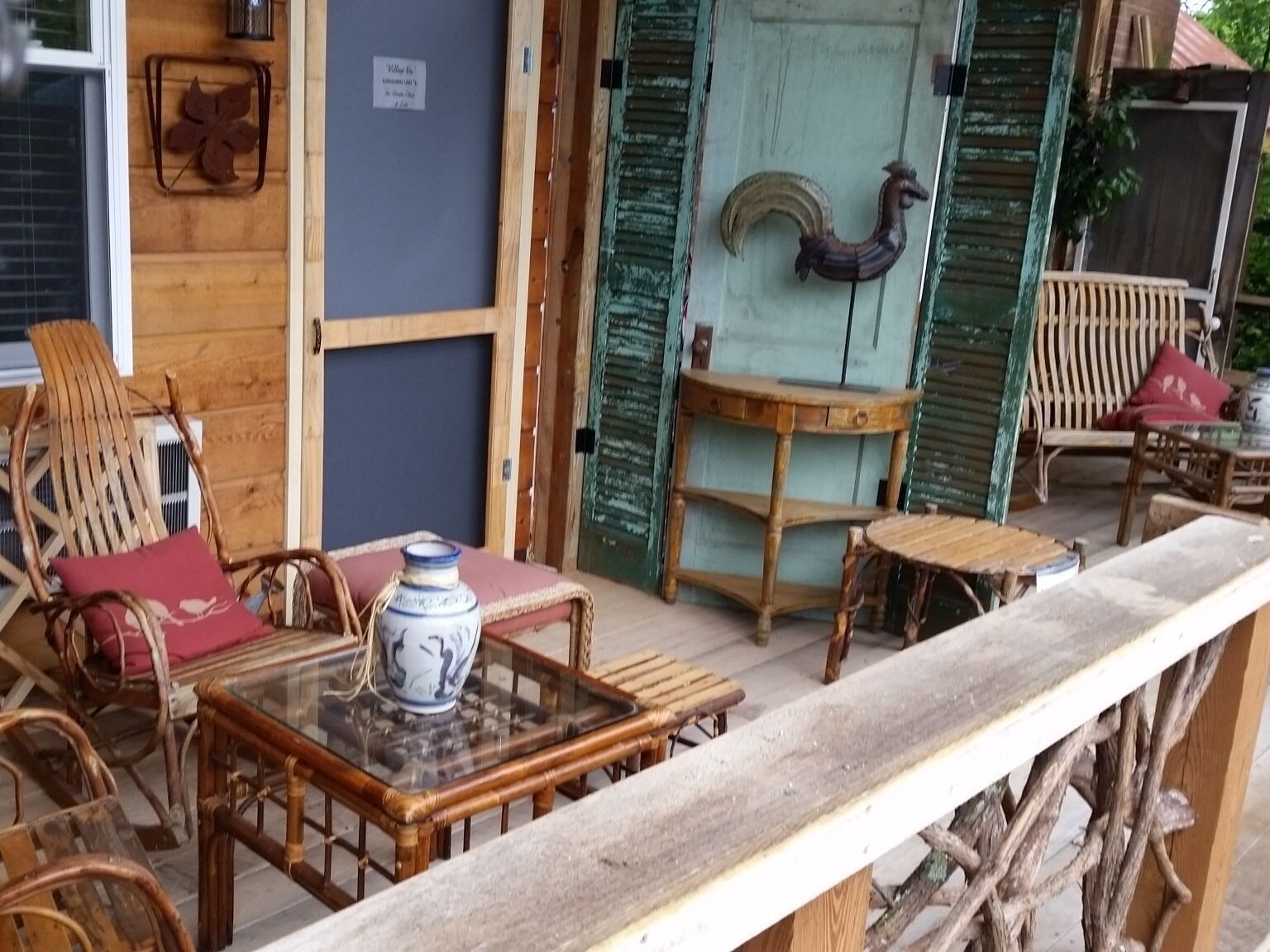 Een rustiek houten terras met rieten meubels, een tafel met glazen blad en een decoratieve vaas.