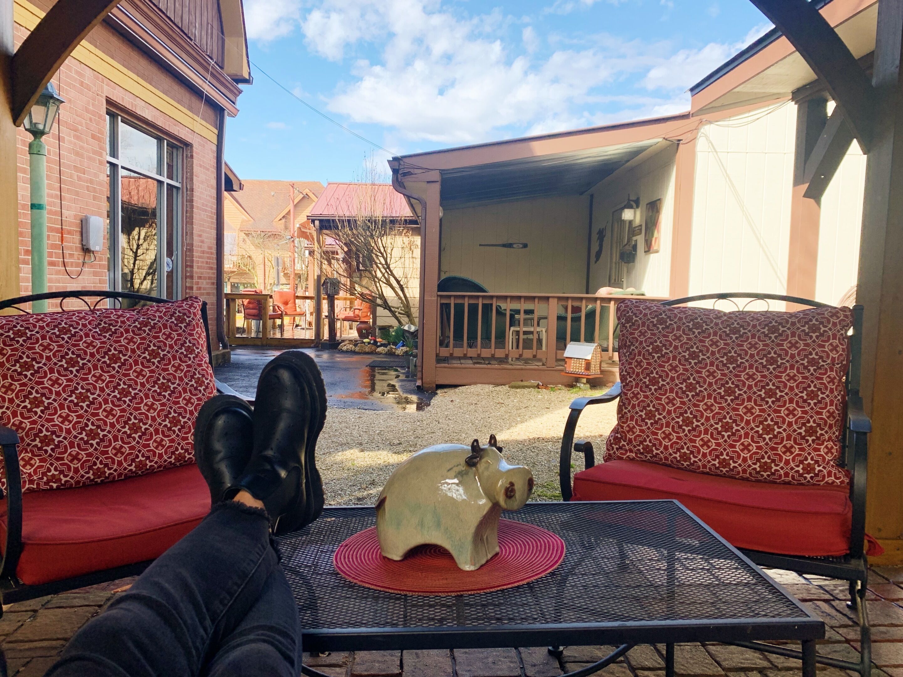 A patio with two red cushioned chairs, a metal table, and a pig-shaped sculpture.