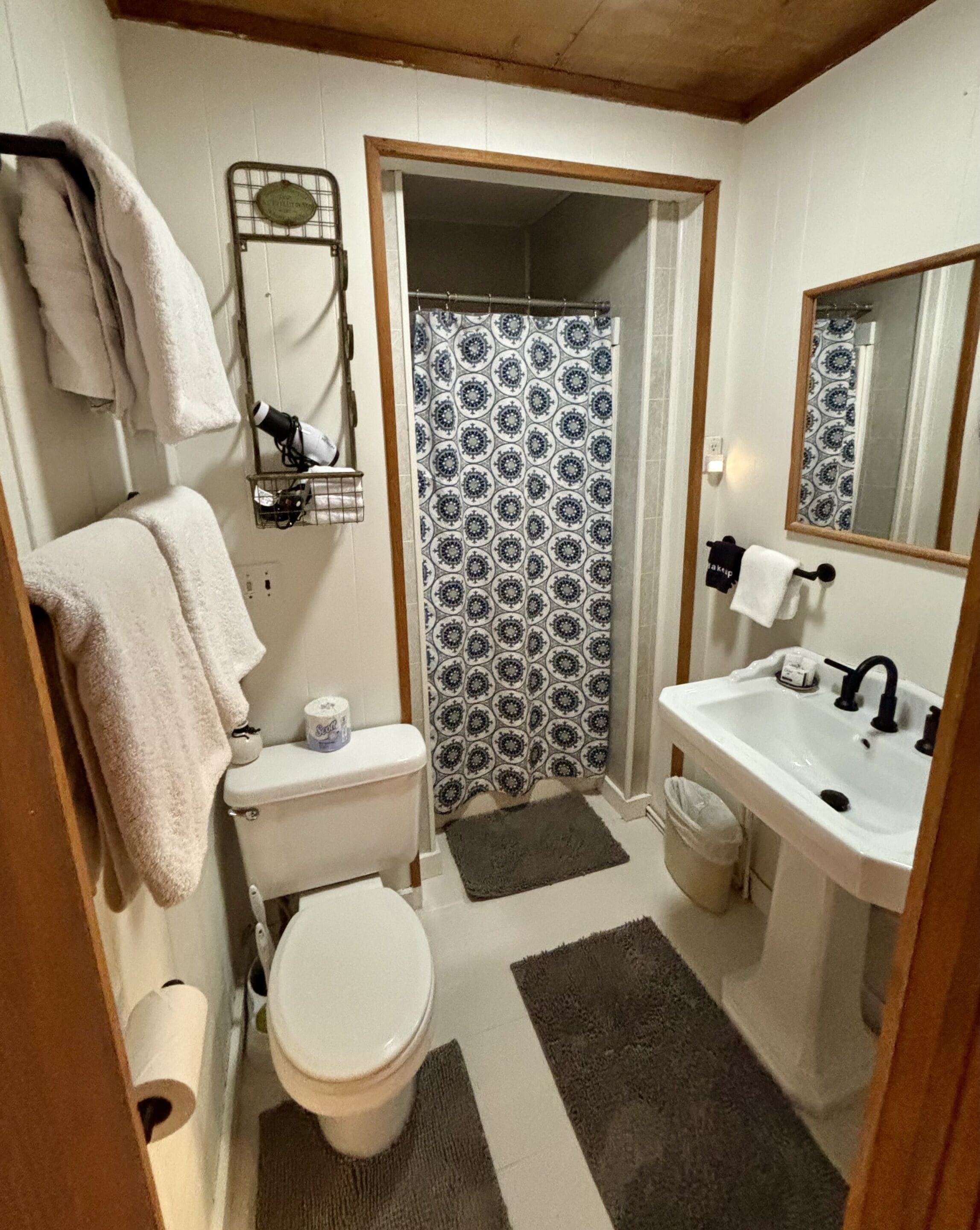 A compact bathroom with a toilet, sink, and shower. There are towels hanging on a rack and a mirror above the sink.
