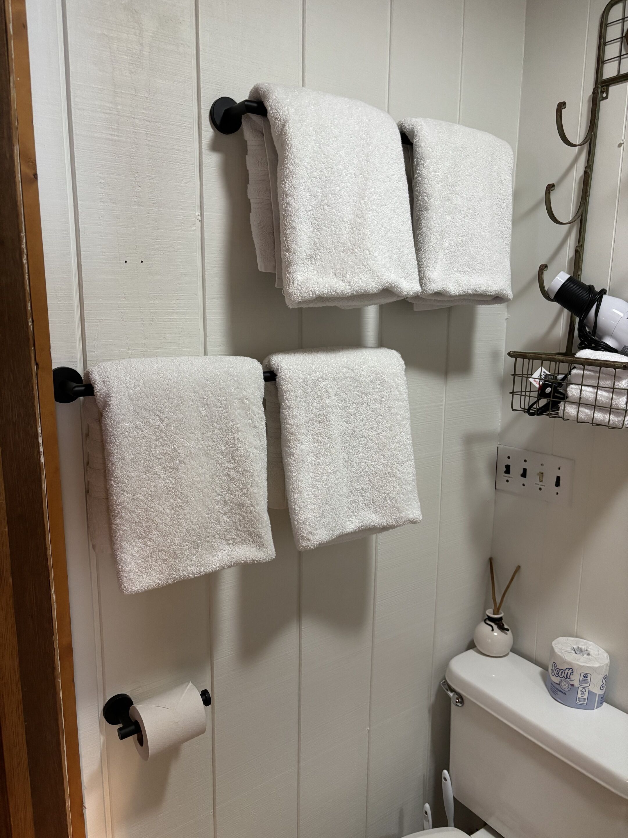 Et badeværelse med hvide håndklæder på en holder, en toiletpapirholder, en hårtørrer og en rulle toiletpapir.