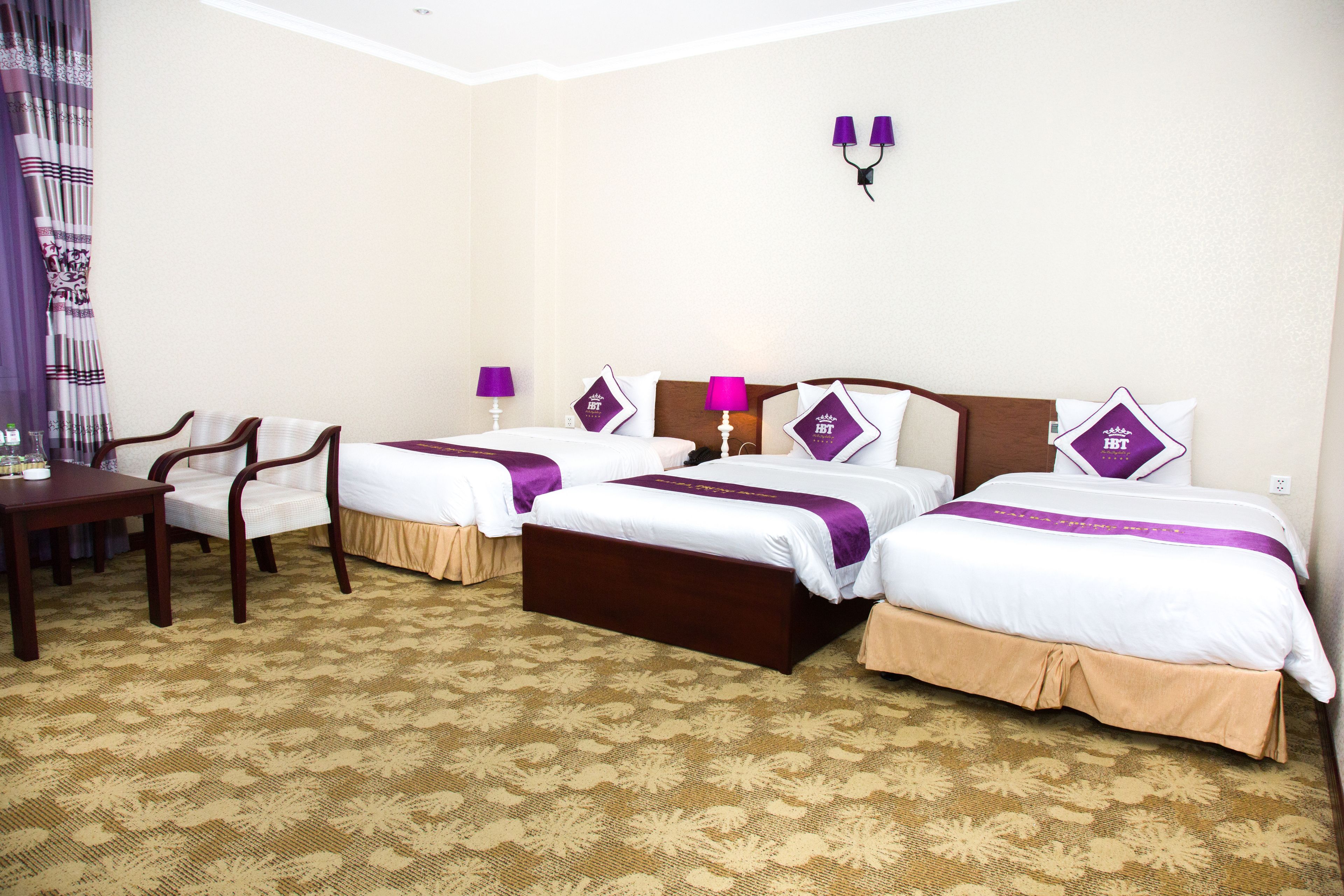 A hotel room with three beds, a wooden desk, and a patterned carpet.