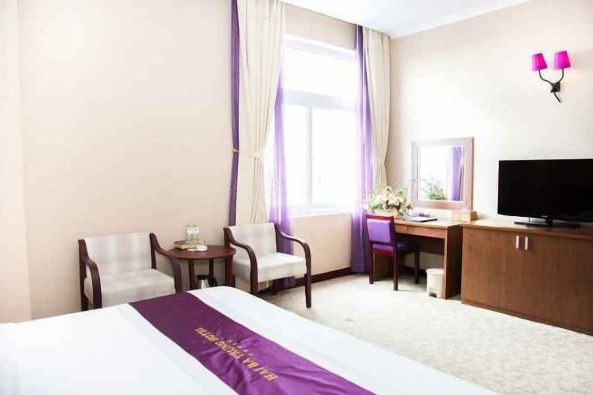 A hotel room with a bed, two armchairs, a desk with a television, and a window with curtains.