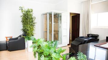 Un salon moderne doté d’un ascenseur en verre, d’un canapé noir, d’une plante en pot et d’un coin repas avec une table et des chaises noires.