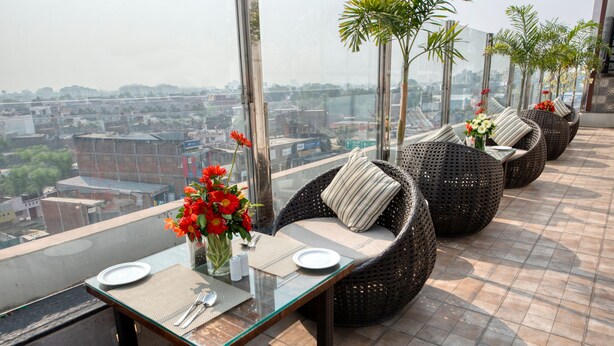 A rooftop terrace with wicker chairs, a glass table, and a view of the cityscape. - Hotel Deep Clarks Inn Lucknow  (Lucknow)