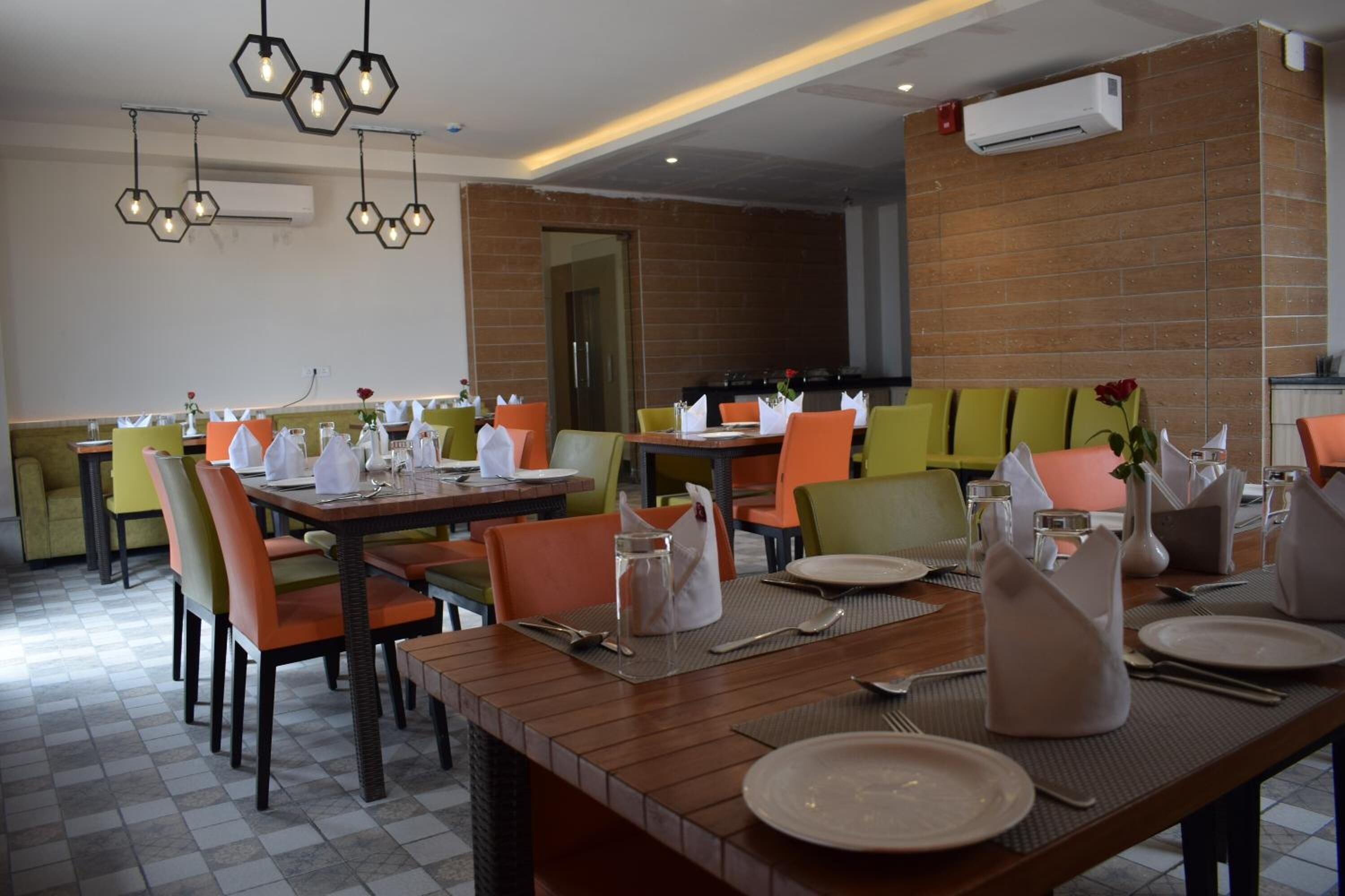 A dining area with multiple tables set for guests, featuring a mix of wooden and cushioned chairs, and a brick wall in the background.