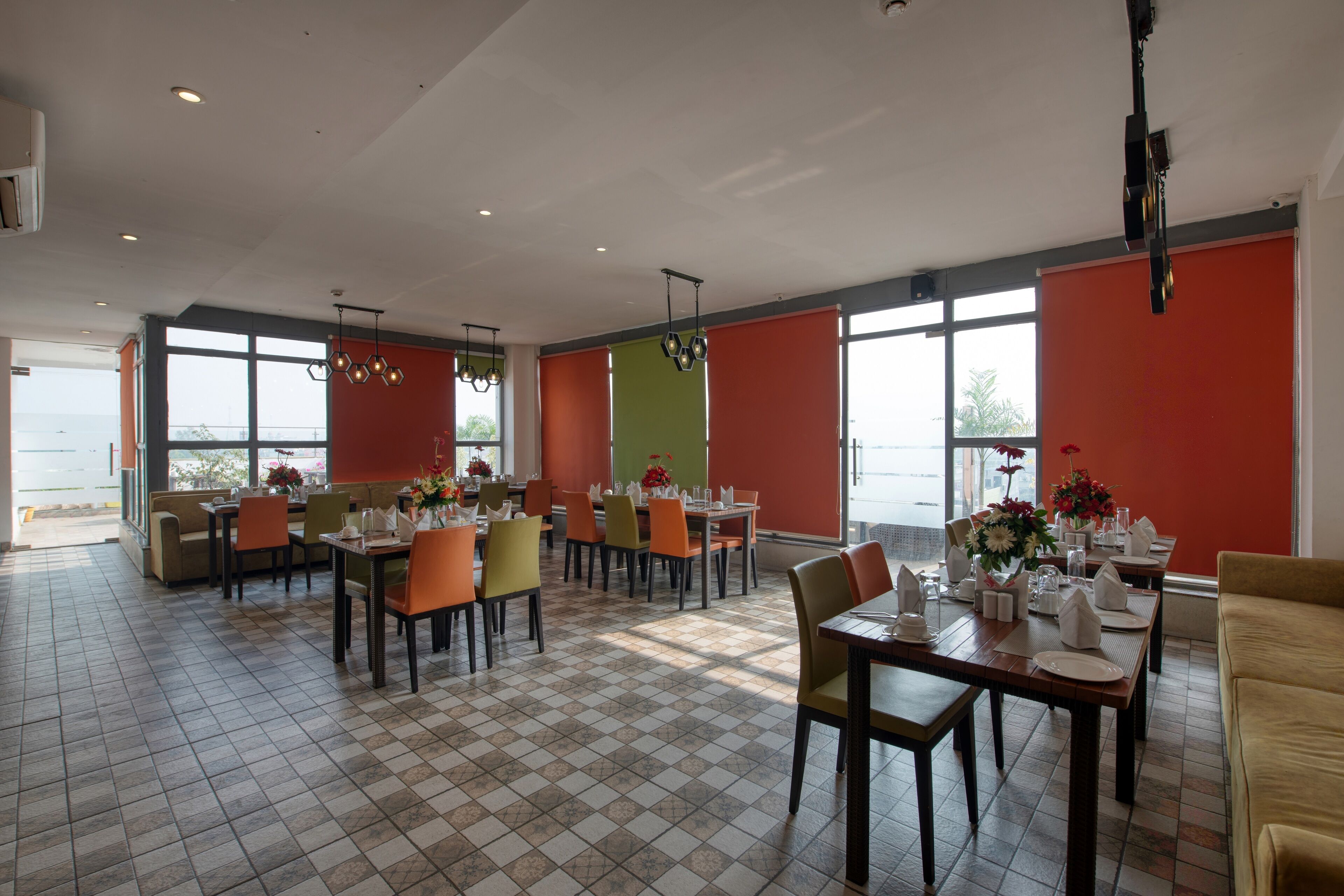 Un vaste espace dédié à la salle à manger, avec de nombreuses tables et chaises, de grandes fenêtres et un sol carrelé.