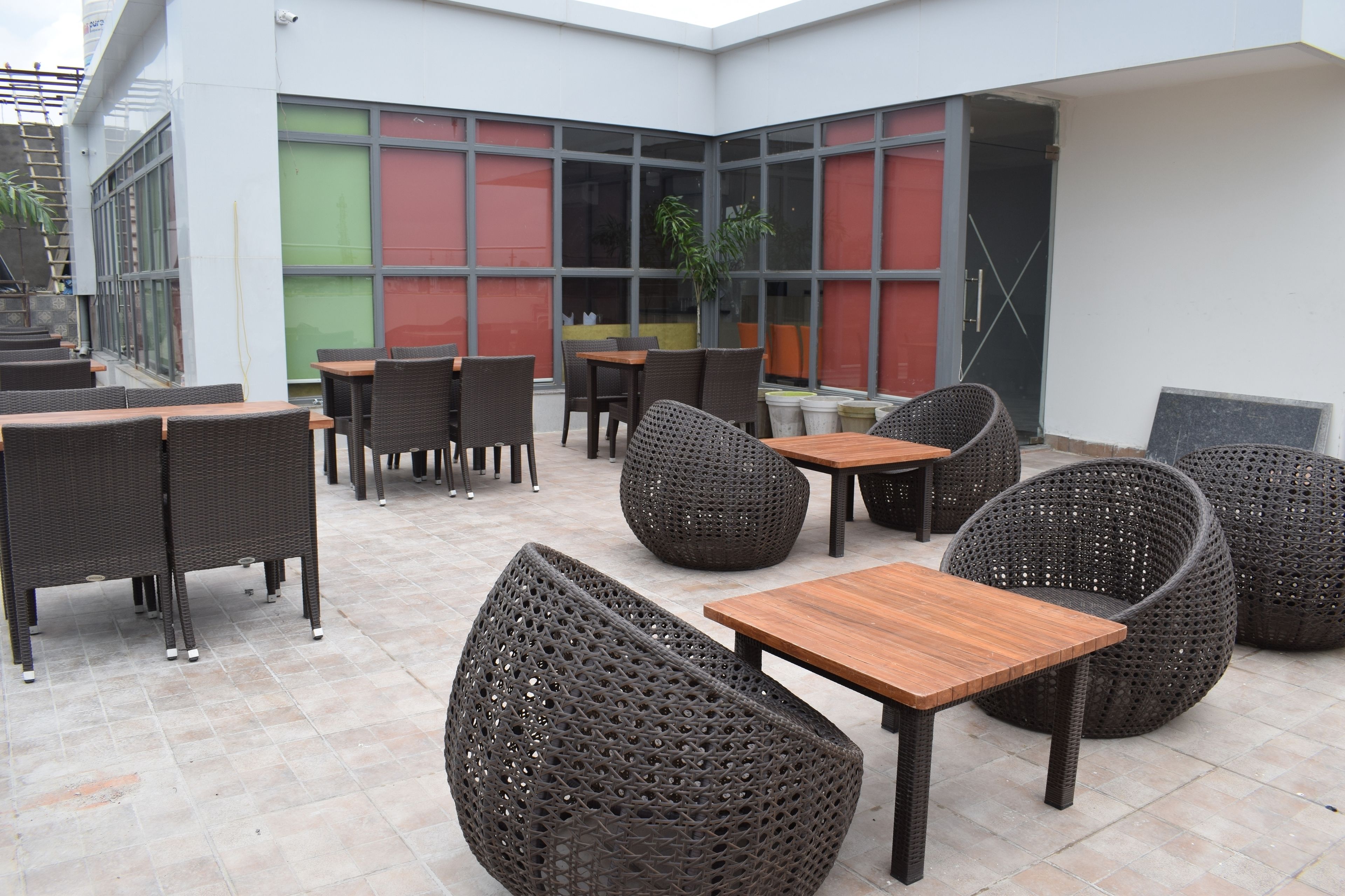 Ein möblierter Patio-Bereich im Freien mit Korbmöbeln, darunter Tische und Stühle, sowie einem großen Pflanzgefäß.