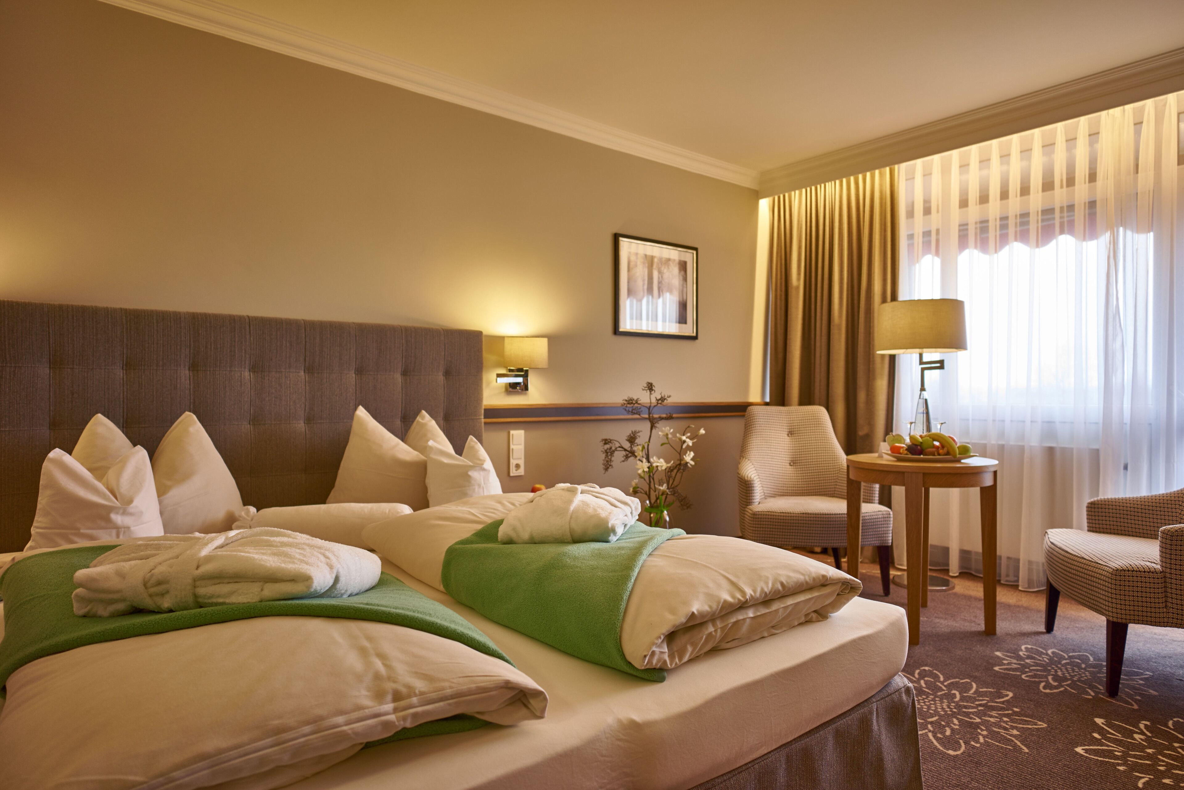 A hotel room with a large bed, a sitting area with a chair and a table, and a window with curtains.