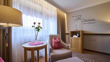 Habitación de hotel con una mesa redonda, una silla con almohada rosa, un armario pequeño y una pared con una frase motivacional.