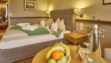 Habitación de hotel con una cama bien hecha, una mesita de noche con una botella y vasos, y un frutero sobre la mesa.