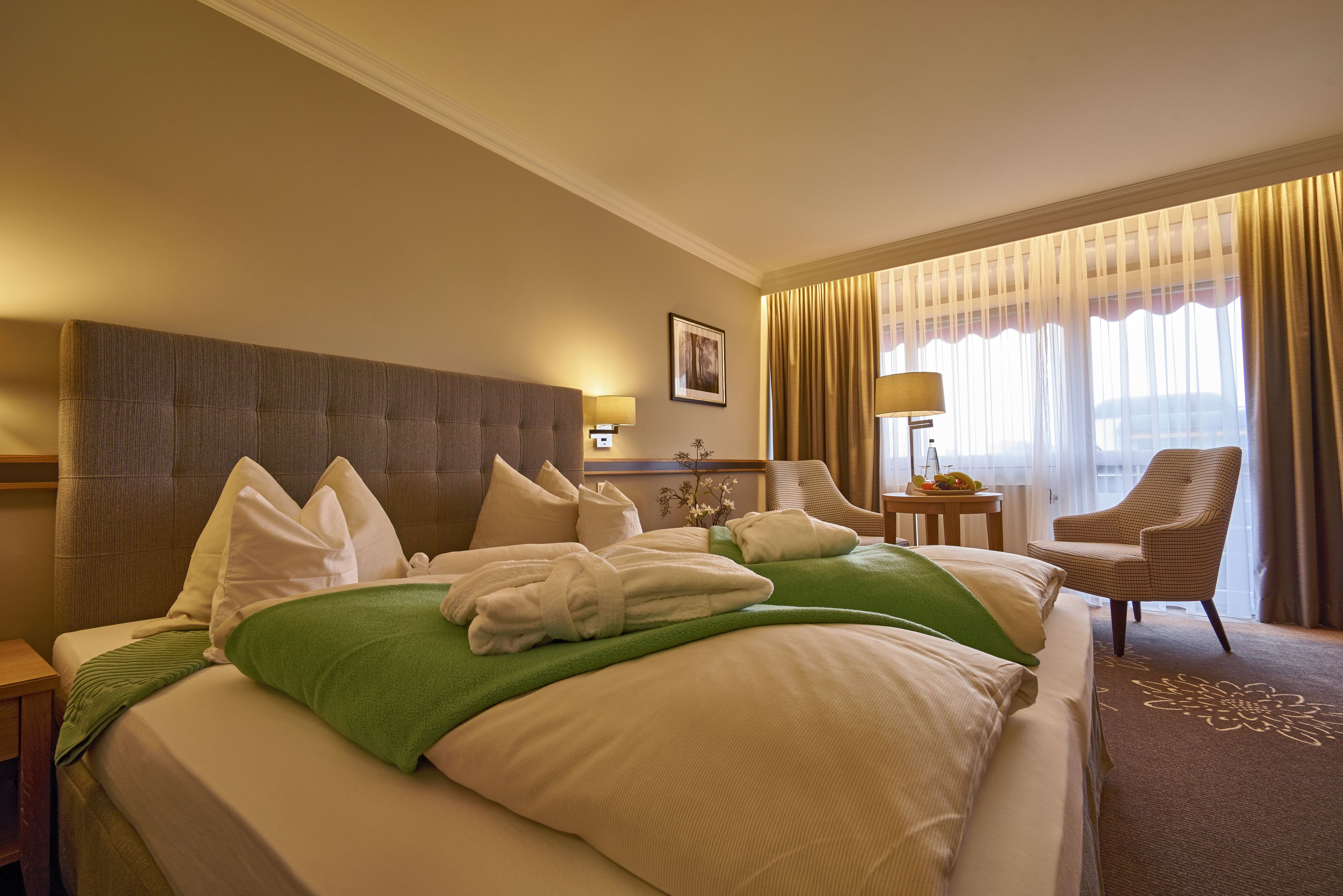 Habitación de hotel con una cama grande, una silla, una mesita y un ventanal con cortinas.