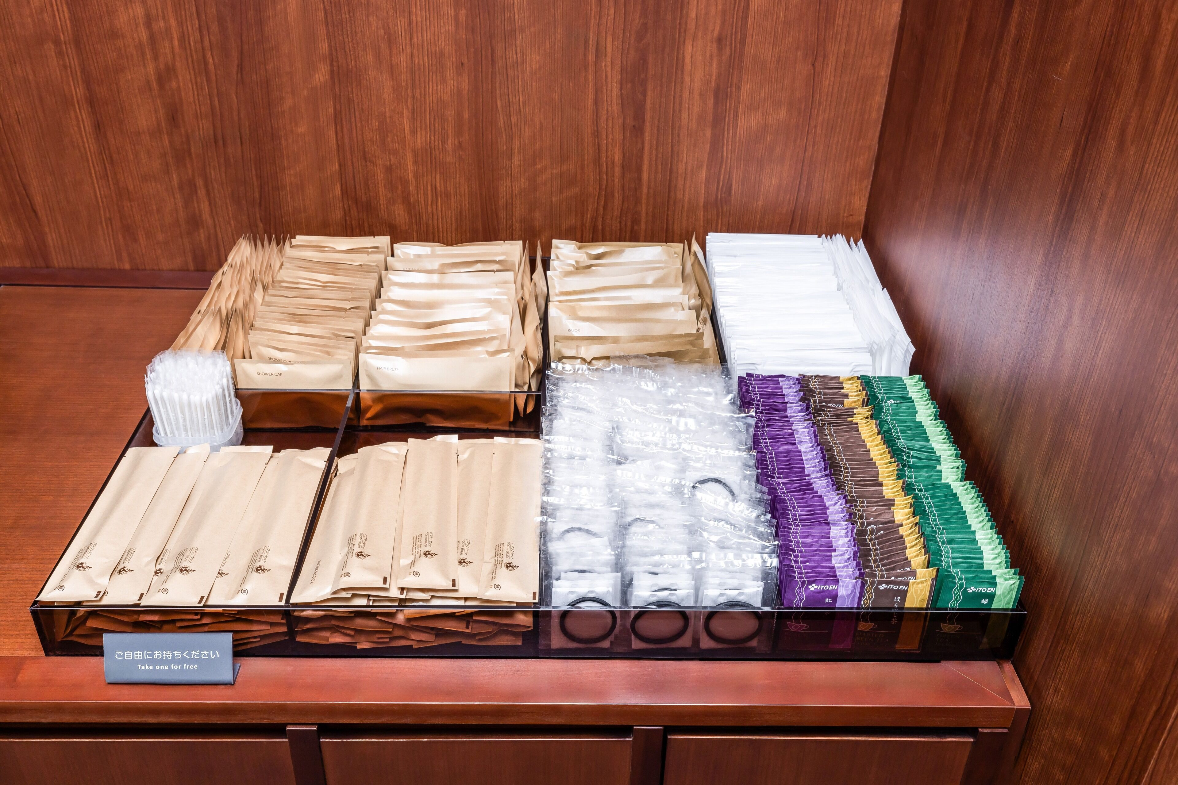 A display of various packaged items, likely toiletries, arranged on a wooden counter with a sign instructing to take one for free.