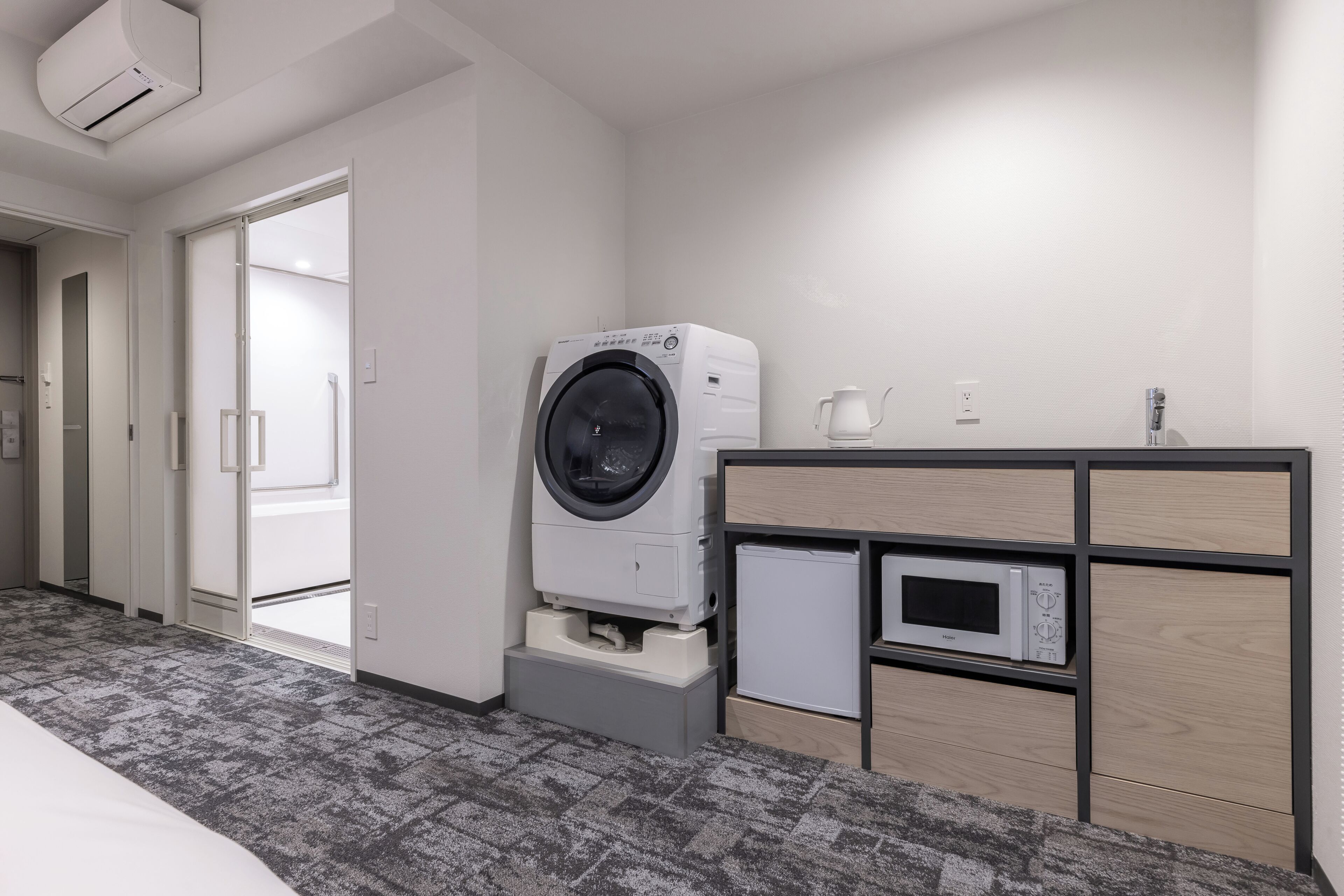 Habitación de hotel con lavadora, microondas, cafetera y un refrigerador pequeño.