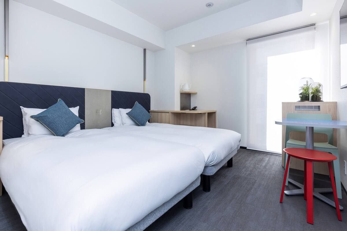 Ein modernes Hotelzimmer mit zwei Betten, einem Schreibtisch und einem Stuhl.