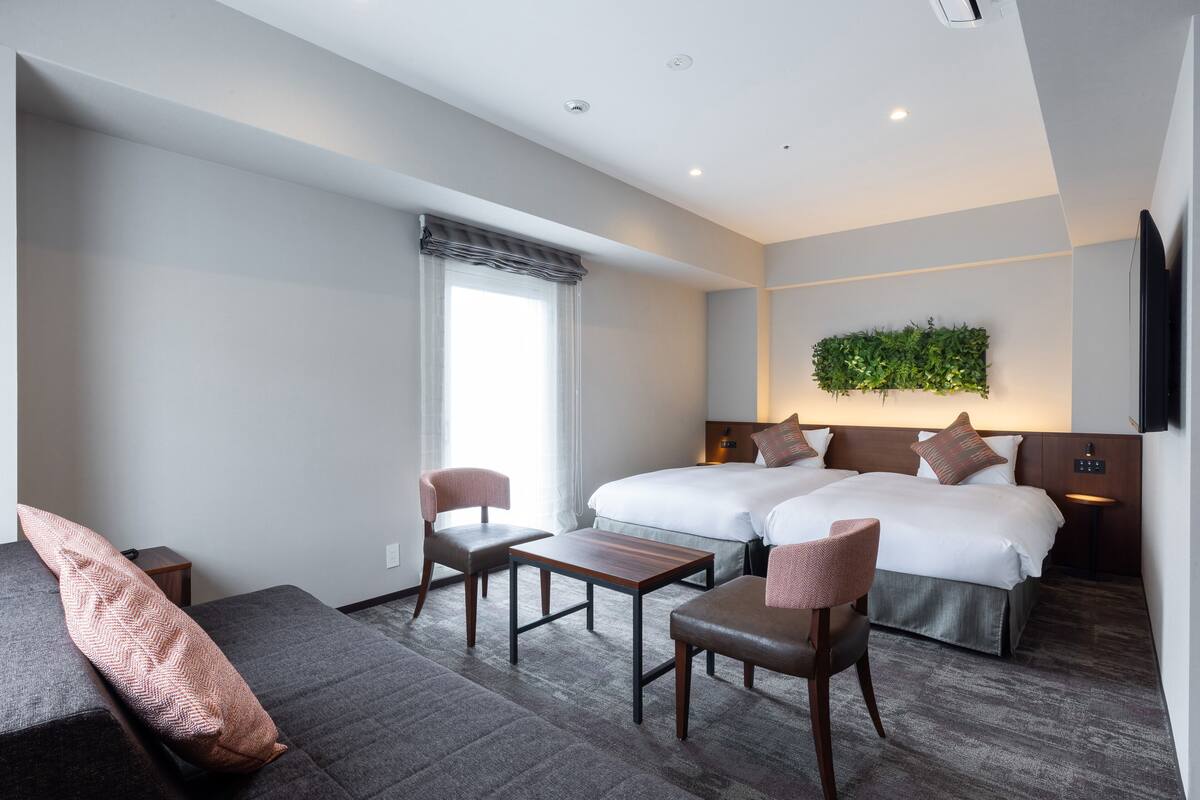 Ein modernes Hotelzimmer mit zwei Betten, einer Couch, einem kleinen Tisch und einem Fernseher.