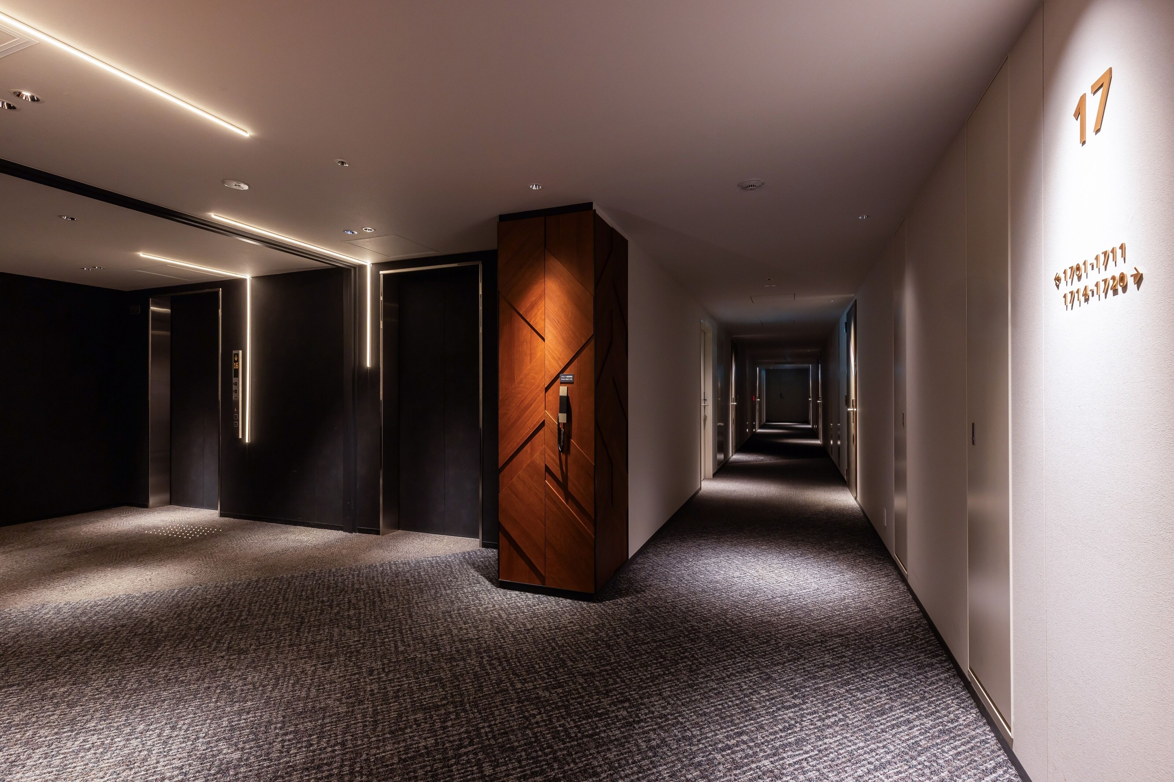 Passadís d'hotel modern amb una columna de fusta central, parets fosques i un sòl amb moqueta.