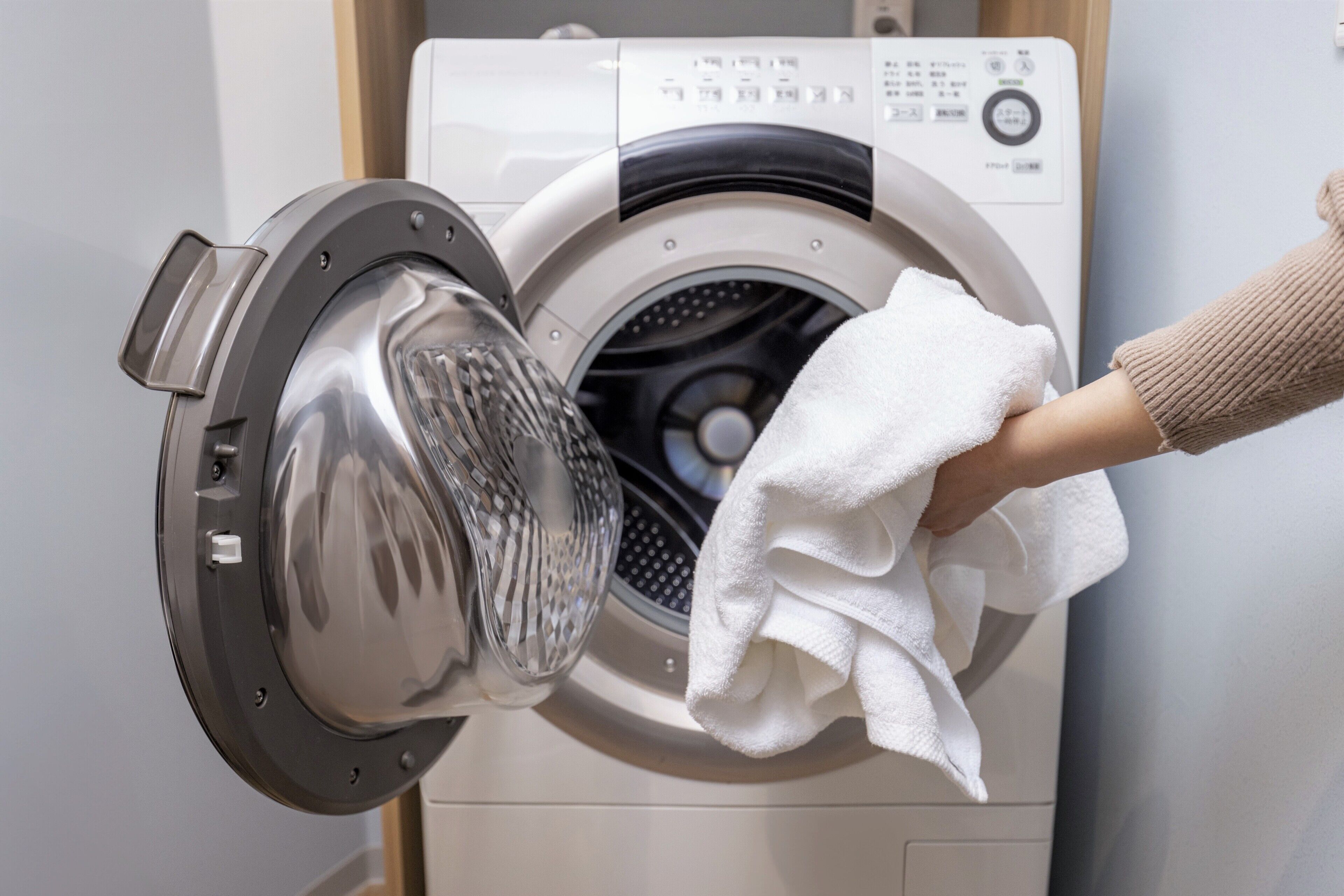 A front-loading washing machine with a hand holding a white cloth in front of it.