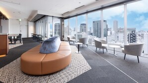 Un espacio de oficina moderno con un amplio ventanal que ofrece vista a la ciudad, una zona de estar curvada y una mesa de reuniones con sillas.