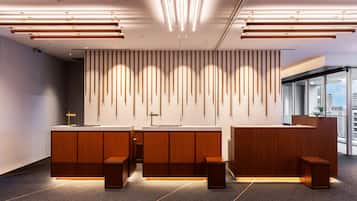 A modern reception area with a wooden reception desk, a cross on the wall, and a city view through large windows.