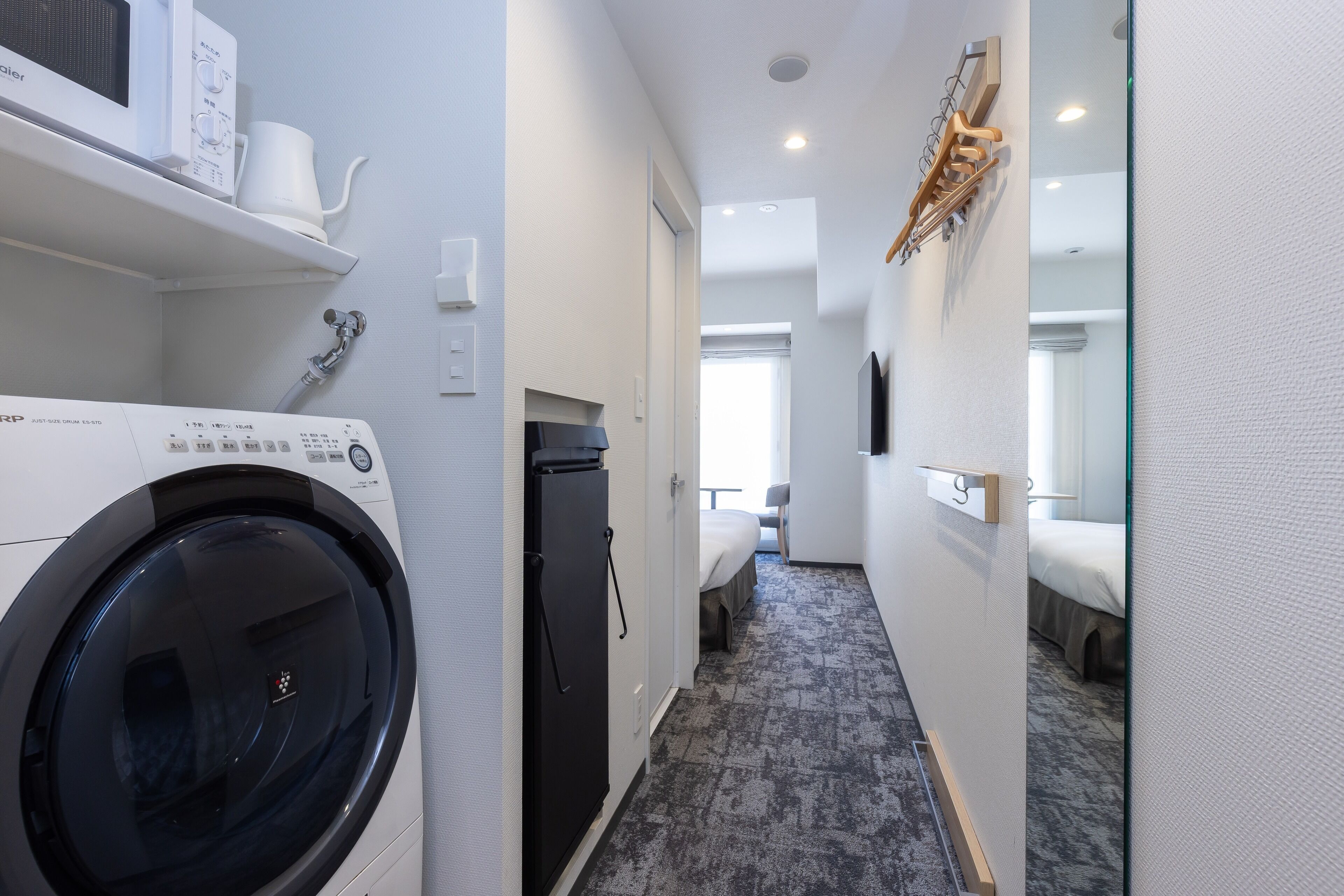 Zona de lavandería con lavadora, secadora y refrigerador. Hay un pasillo que conduce a un dormitorio con cama y ventana.