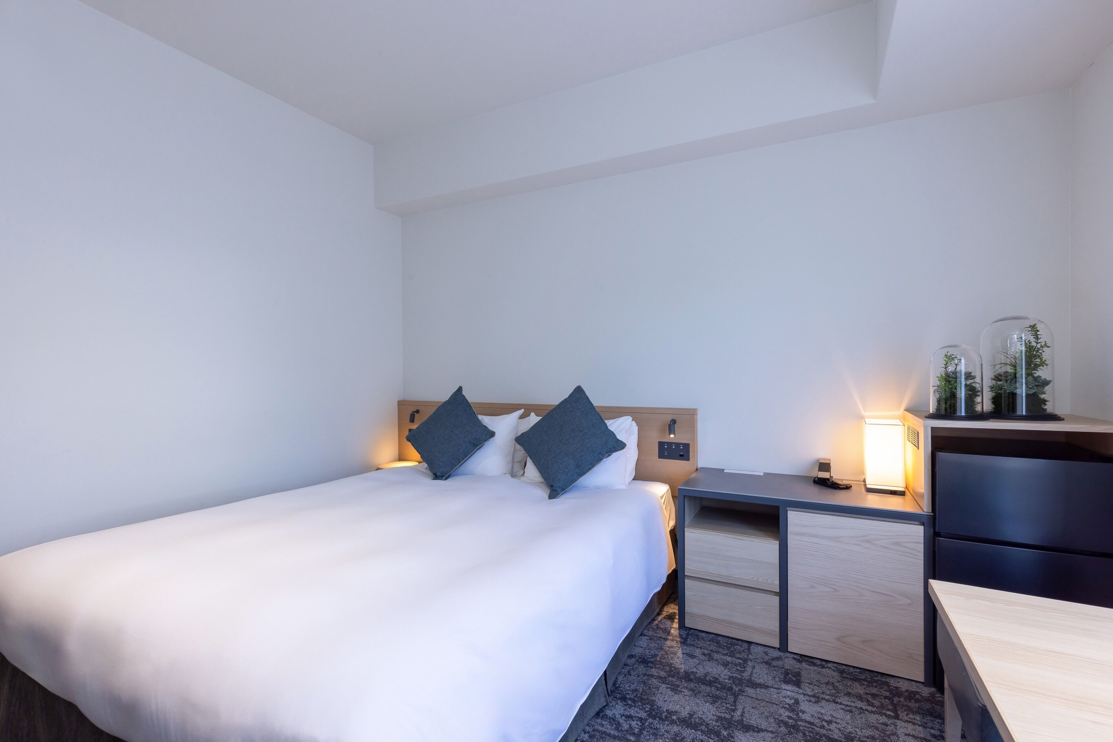 Una habitación de hotel con cama, mesitas de noche, escritorio y lámpara.
