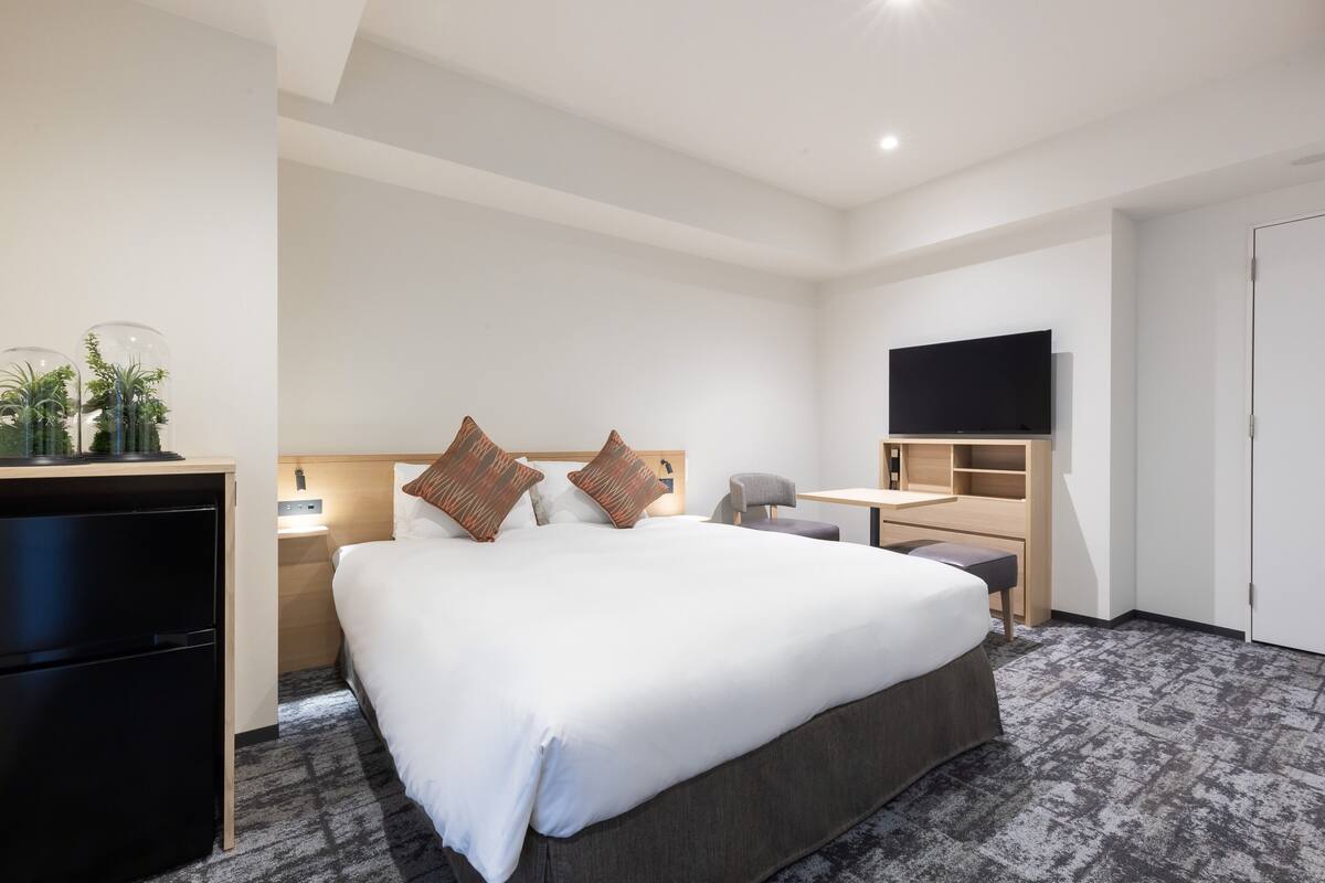 Ein Hotelzimmer mit einem großen Bett, einem Schreibtisch, einem Fernseher und einer Minibar.