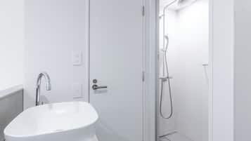 A modern bathroom with a white sink, a shower with a handheld showerhead, and a door leading to another room.