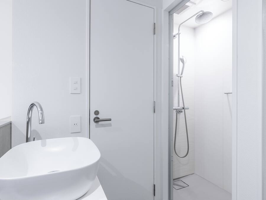 A modern bathroom with a white sink, a shower with a handheld showerhead, and a door leading to another room.
