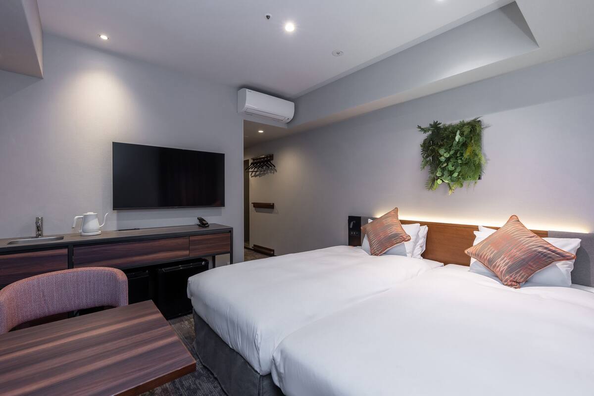 Ein modernes Hotelzimmer mit einem großen Bett, einem Schreibtisch mit Fernseher, einer Kaffeemaschine und einer kleinen Sitzecke.