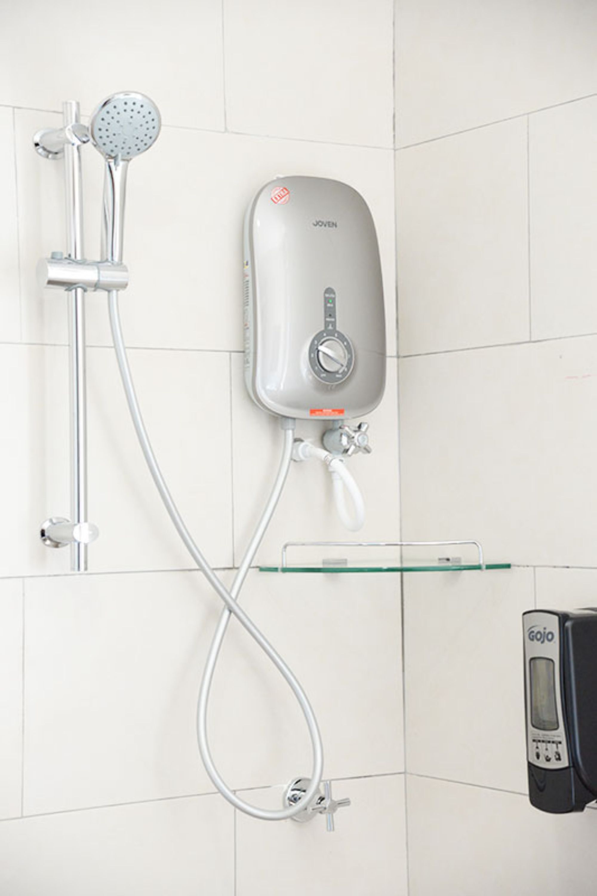 A shower with a handheld showerhead, a wall-mounted soap dispenser, and a handheld soap dispenser.