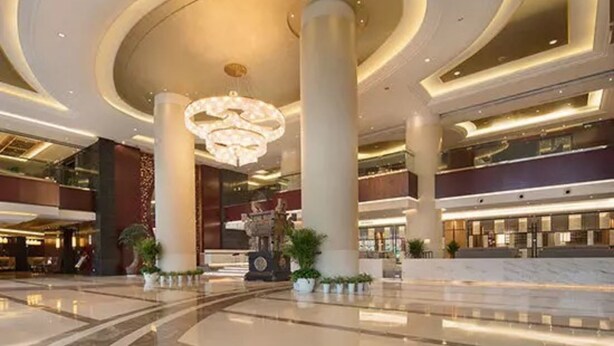 Eine geräumige Lobby mit hoher Decke, großen Säulen und einem zentralen Kronleuchter.