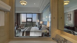 Ein modernes Hotelbad mit einer großzügigen Badewanne, einer Spiegelwand und Blick auf ein Schlafzimmer mit Bett und Schreibtisch.