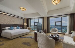 A hotel room with a large bed, a TV, a sofa, and a view of the city.