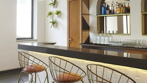 A modern bar area with three bar stools, pendant lighting, and a bar counter with glasses and bottles.