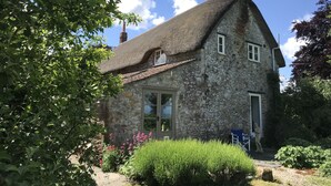 A stone house with a thatched roof, a chimney, and a garden with flowers and shrubs.