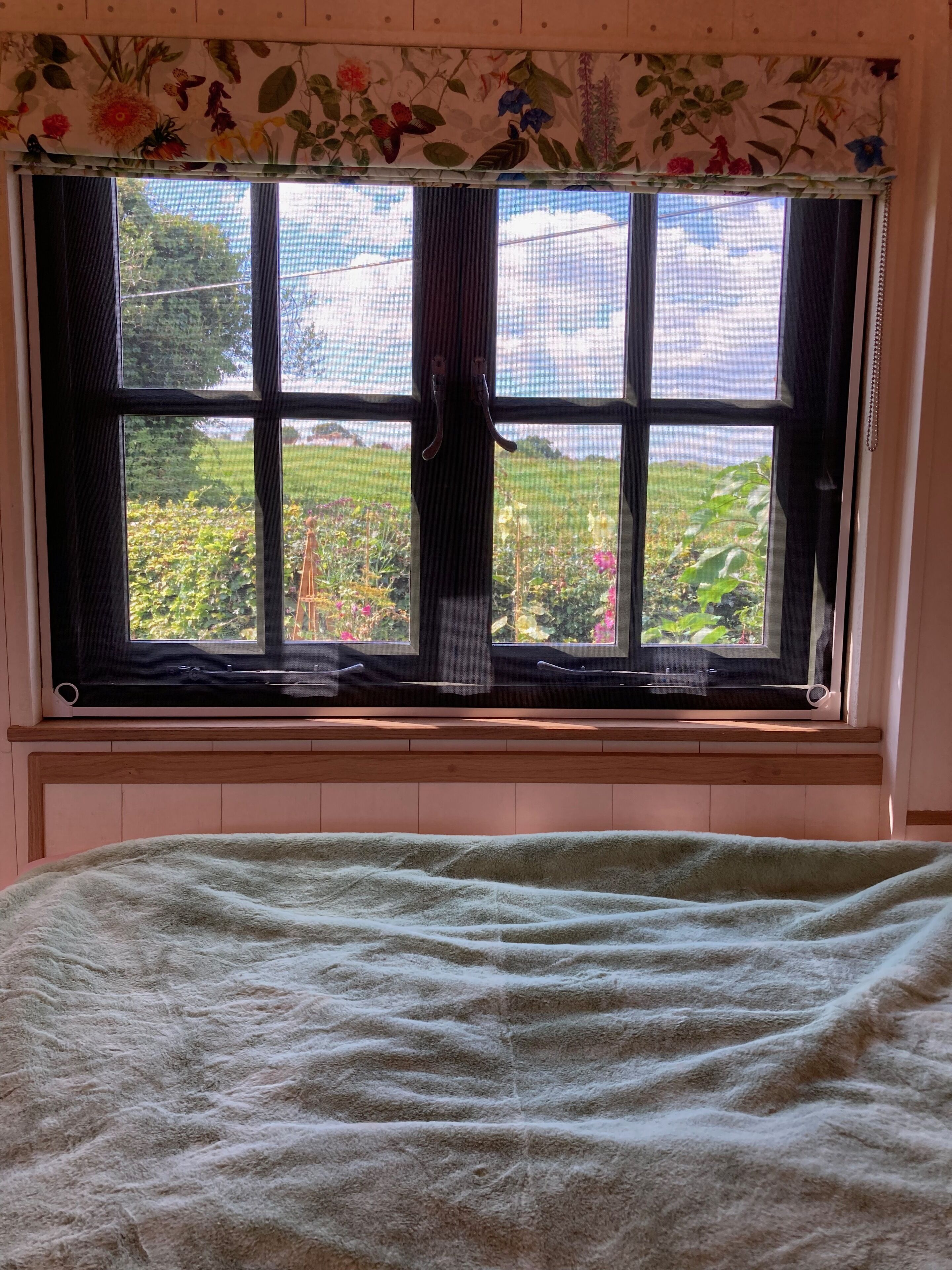 A bedroom with a large window, a bed, and a floral curtain.