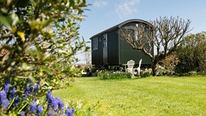 A green building with a curved roof, surrounded by a well-maintained garden with flowers and a white chair.